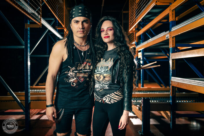 Melany Wild avec Franky Costanza en tenue rock dans un entrepôt industriel, lumière de scène et look Def Leppard, photo par Julien Zannoni